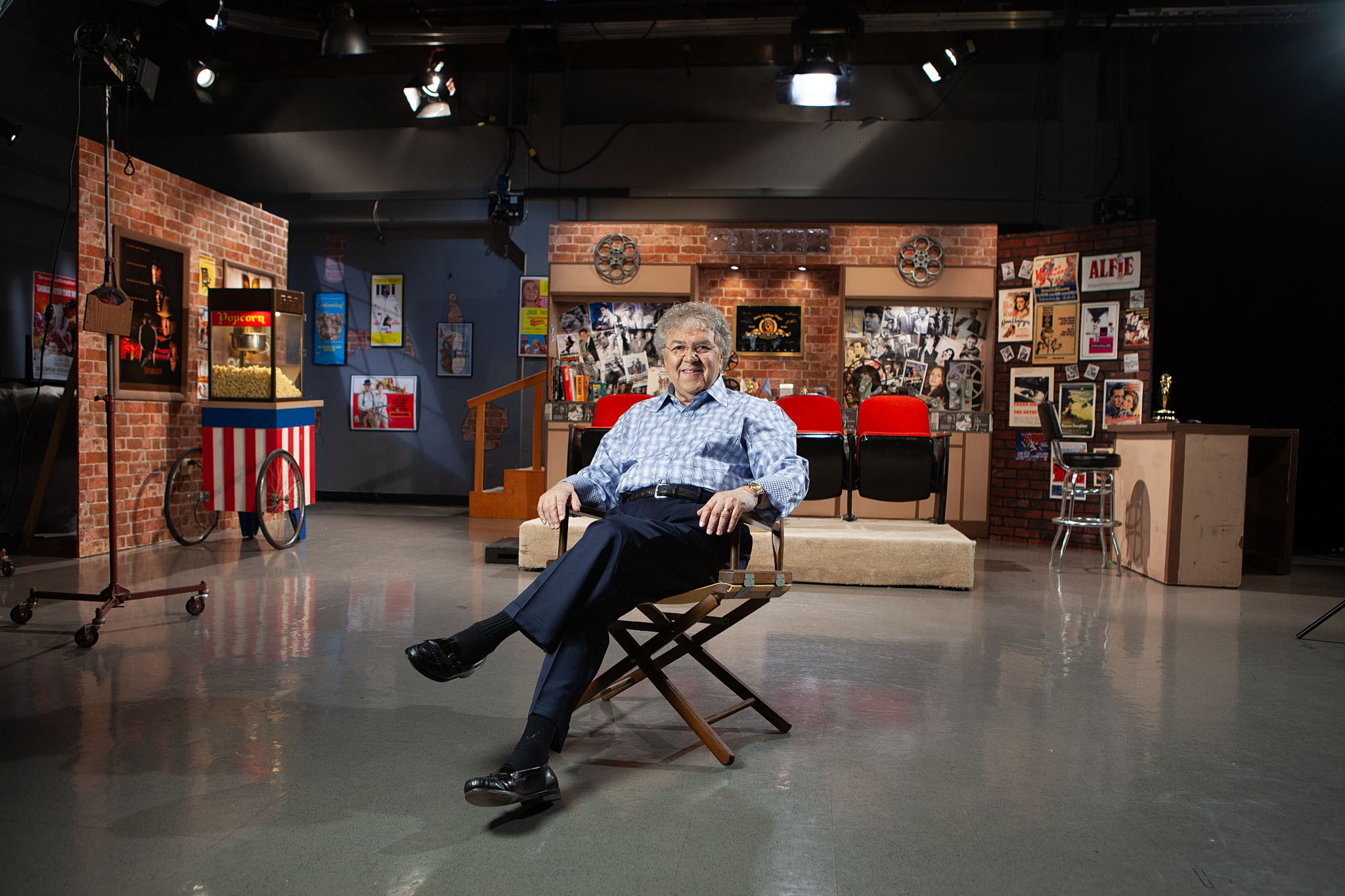 Man seated in a director's chair on a television studio set