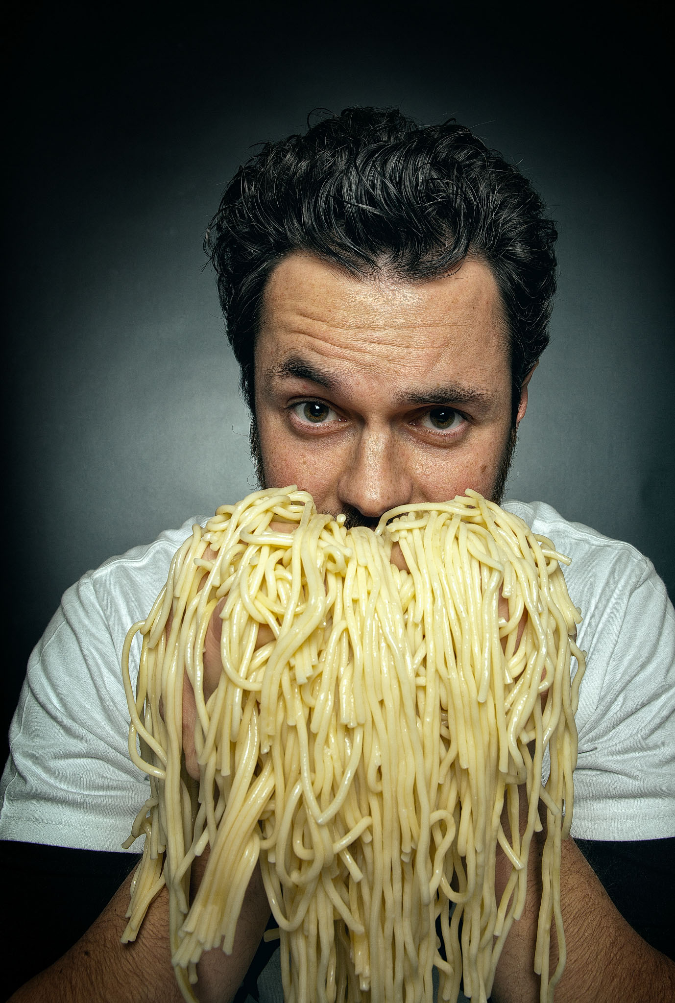 Man holding a mass of spaghetti under his nose like a beard against a dark backdrop
