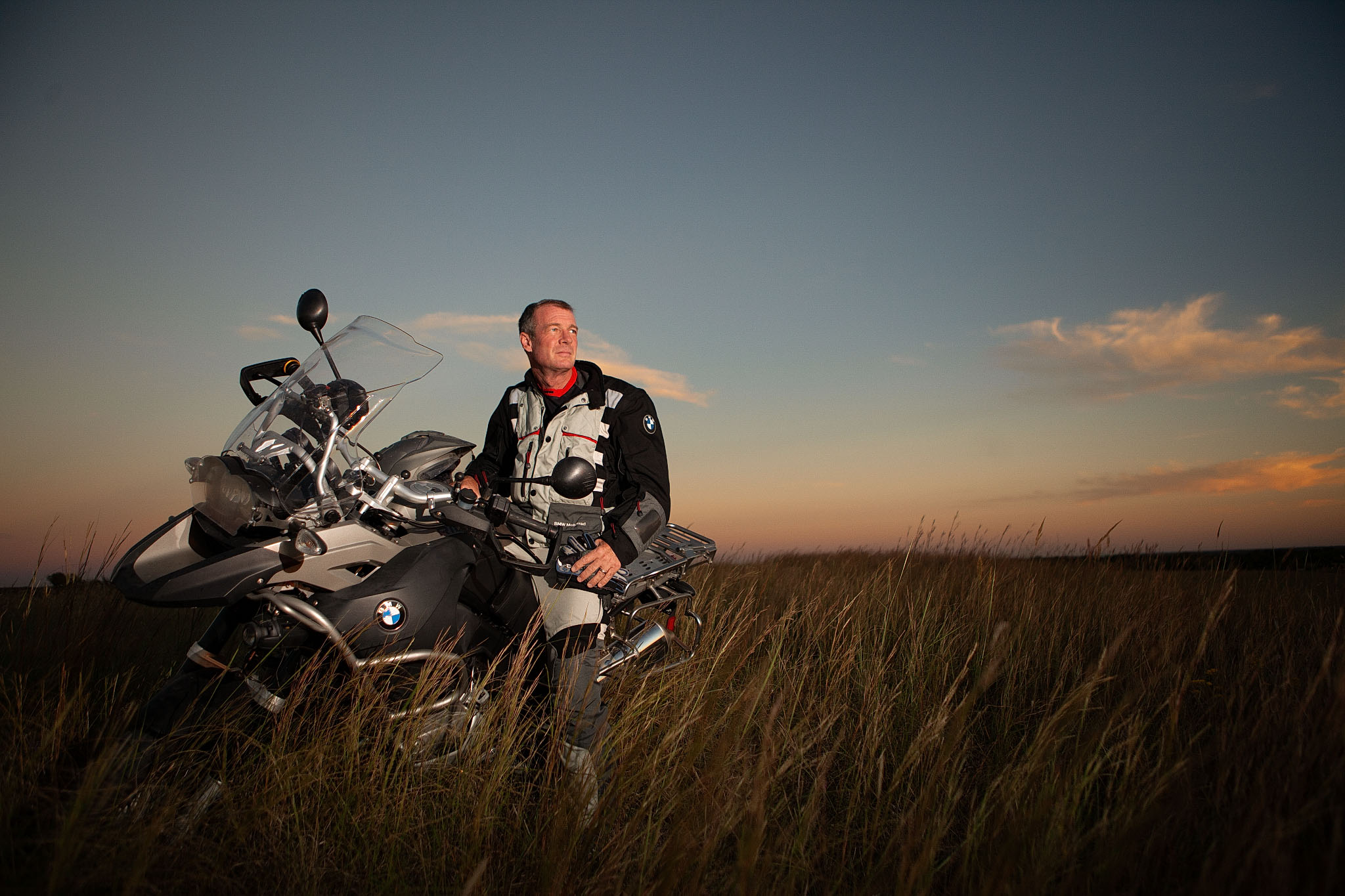 Motorcyclist standing beside an adventure motorcycle in a prairie at sunset