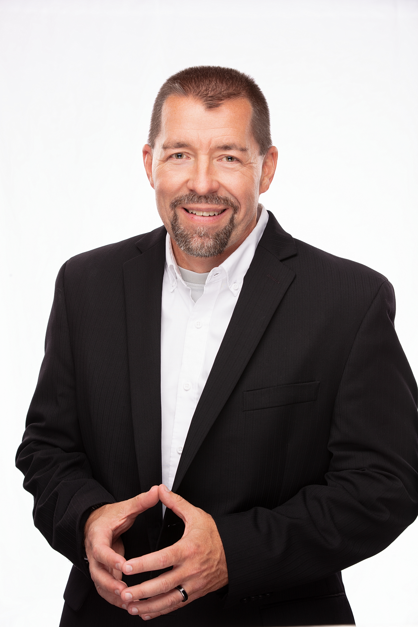 Business headshot of a smiling man in a black suit jacket and white shirt on a white backdrop