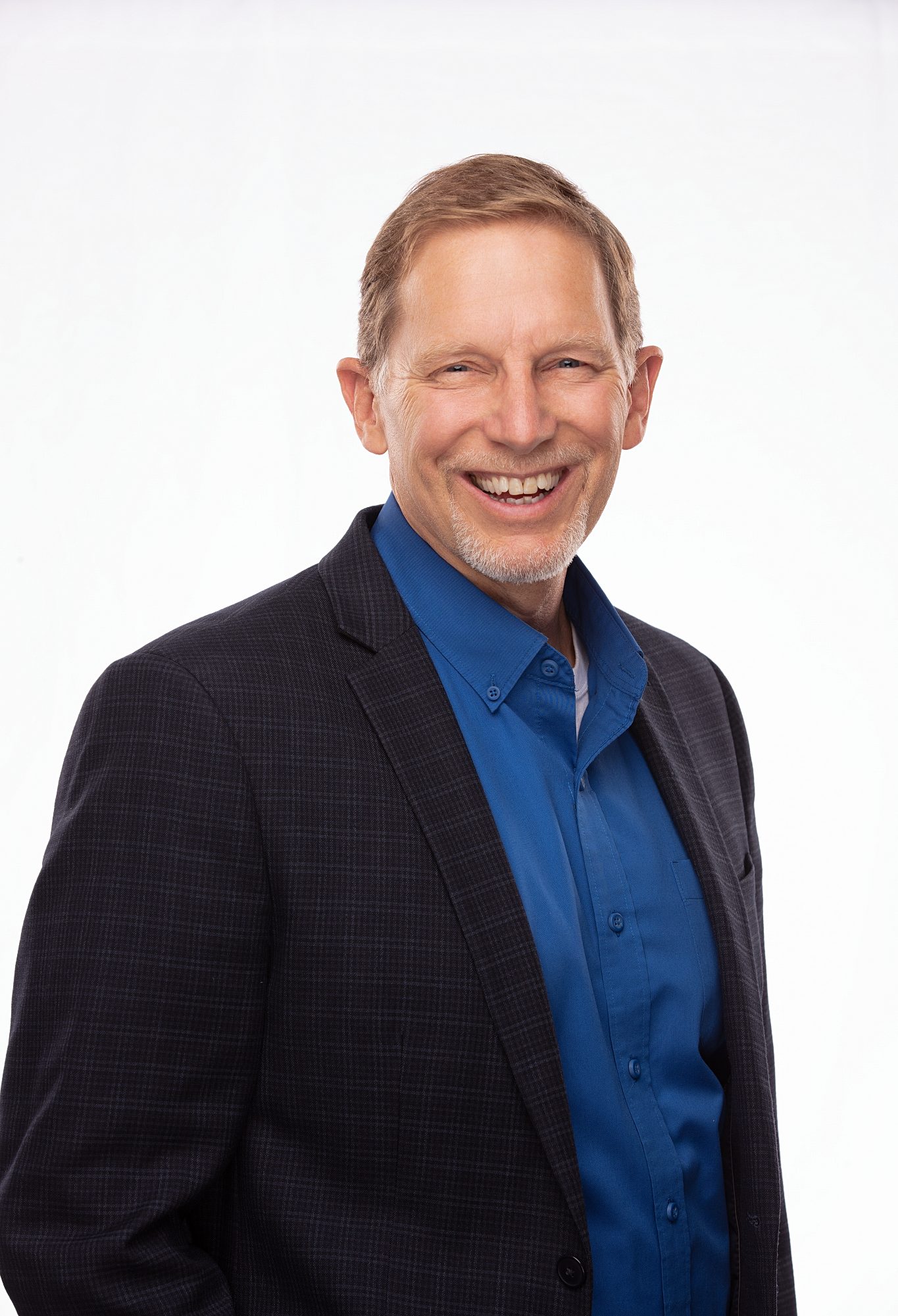 Business headshot of a smiling man in a navy blazer and blue shirt on a white backdrop