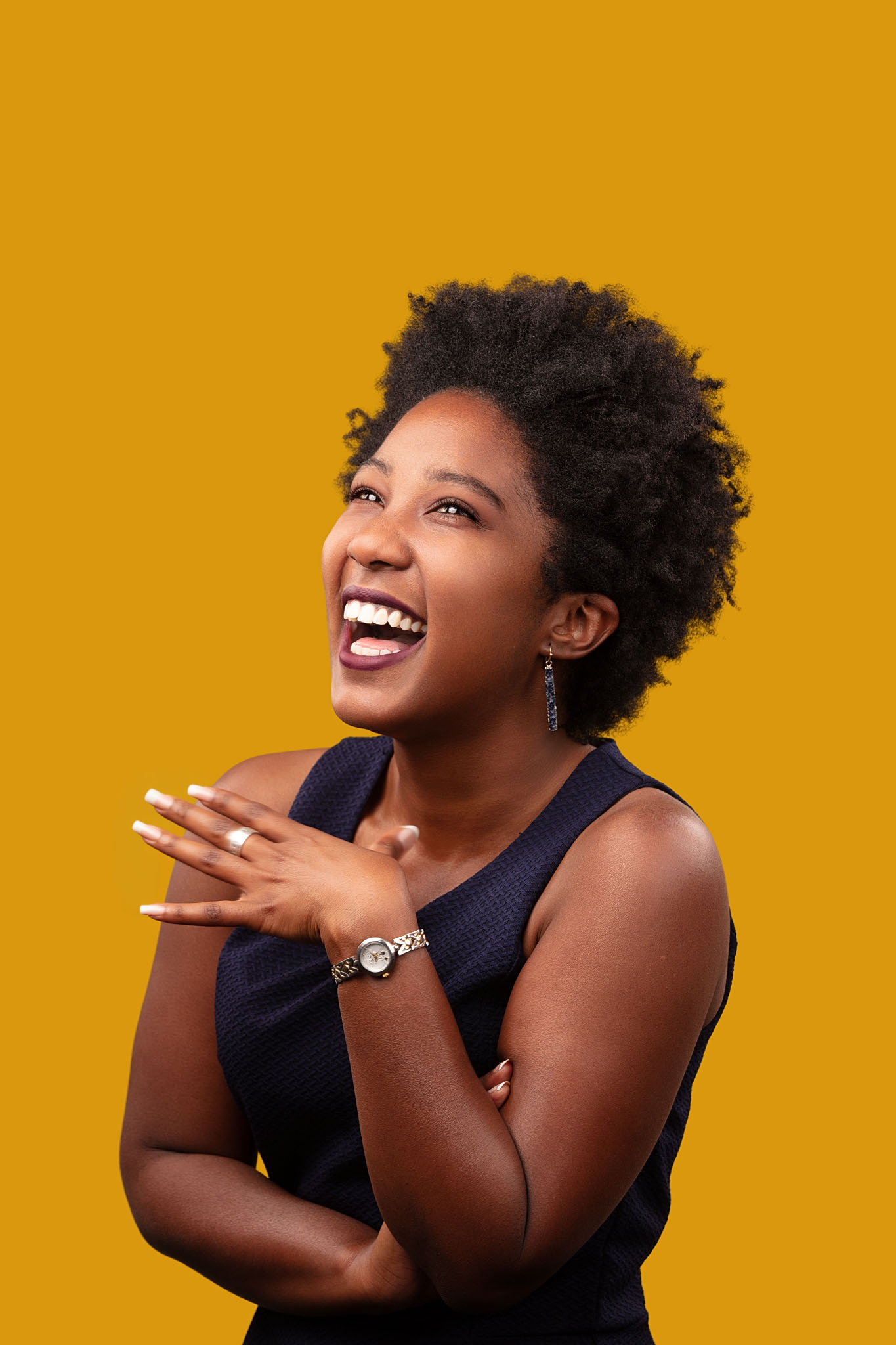 Expressive studio portrait of a laughing woman in a navy sleeveless top against a gold backdrop