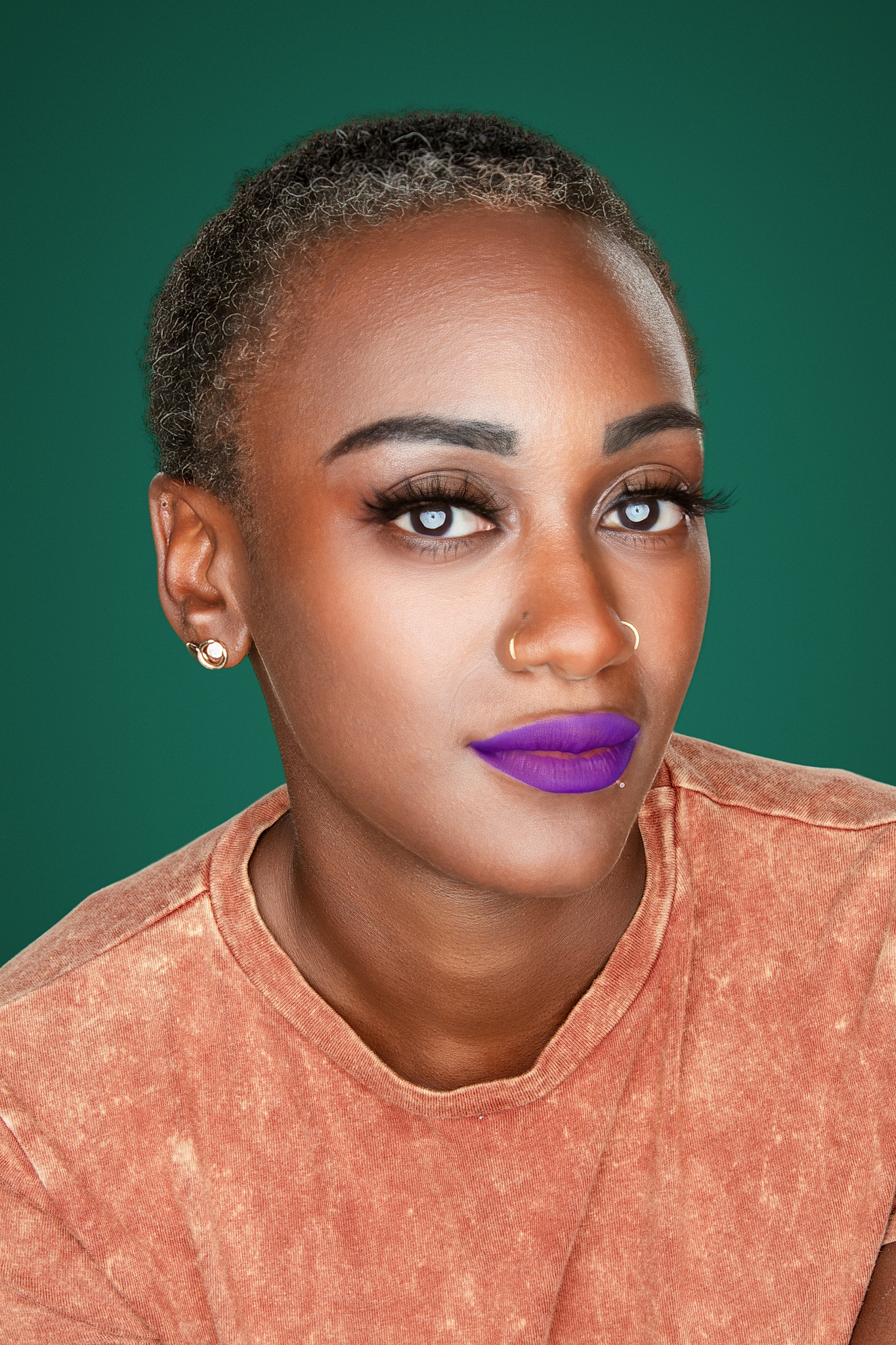 Studio headshot of a woman with purple lipstick in a coral top against a deep green backdrop