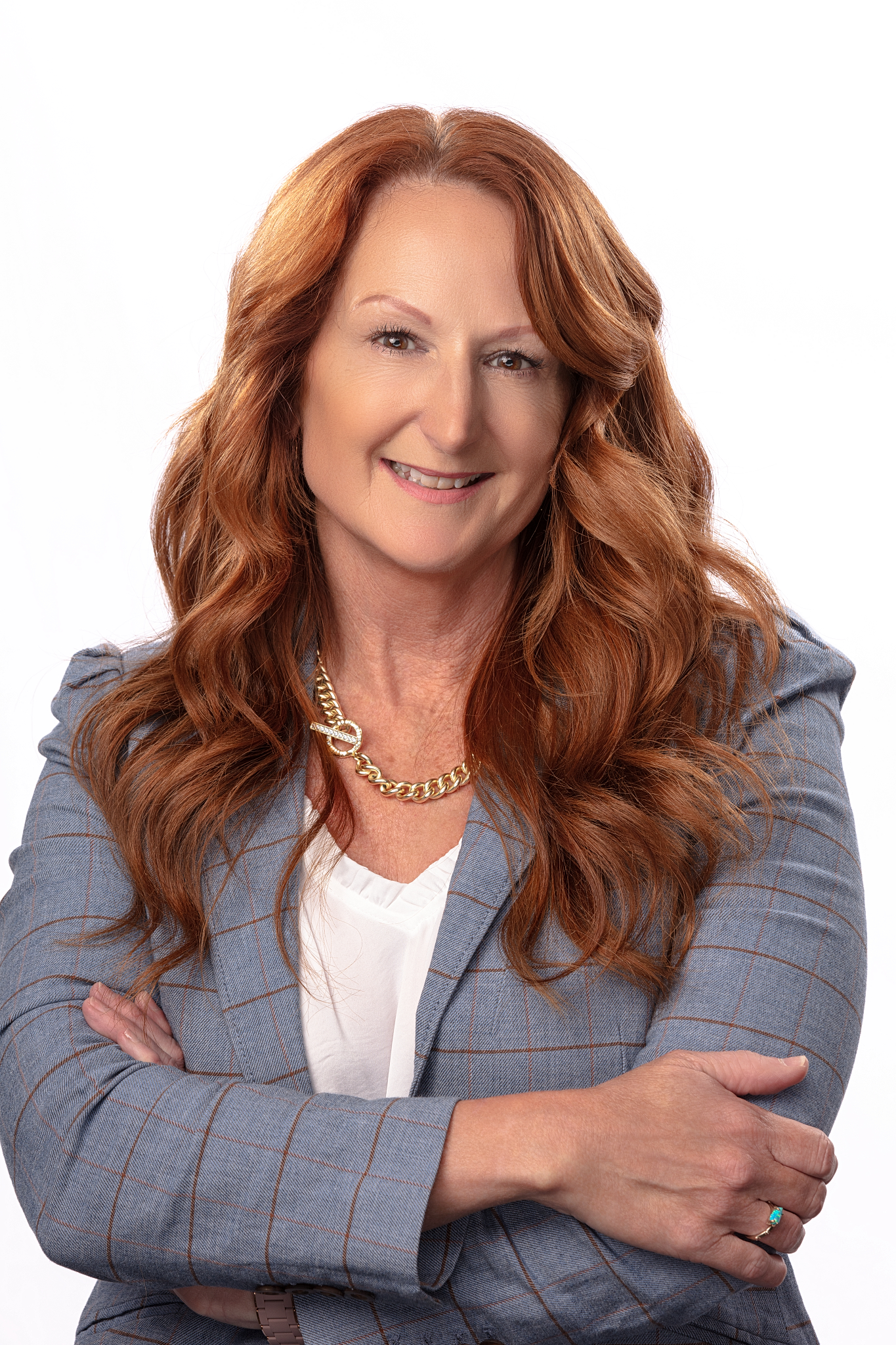 Professional headshot of a woman with long red hair in a gray plaid blazer, arms crossed, on a white backdrop