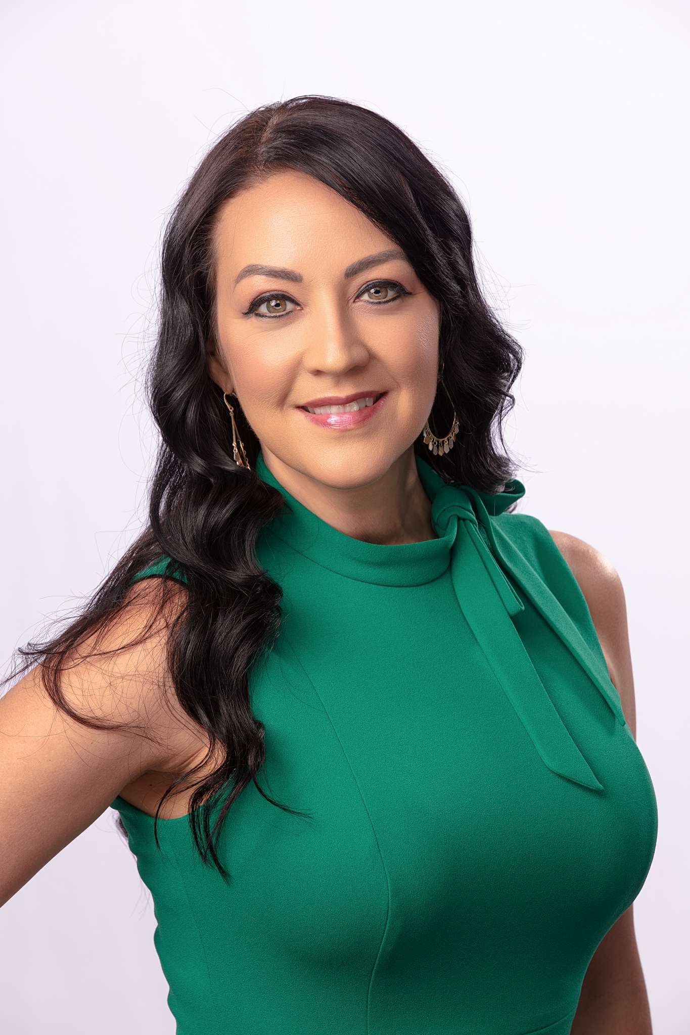 Professional headshot of a woman with long dark hair in a green sleeveless top on a white backdrop