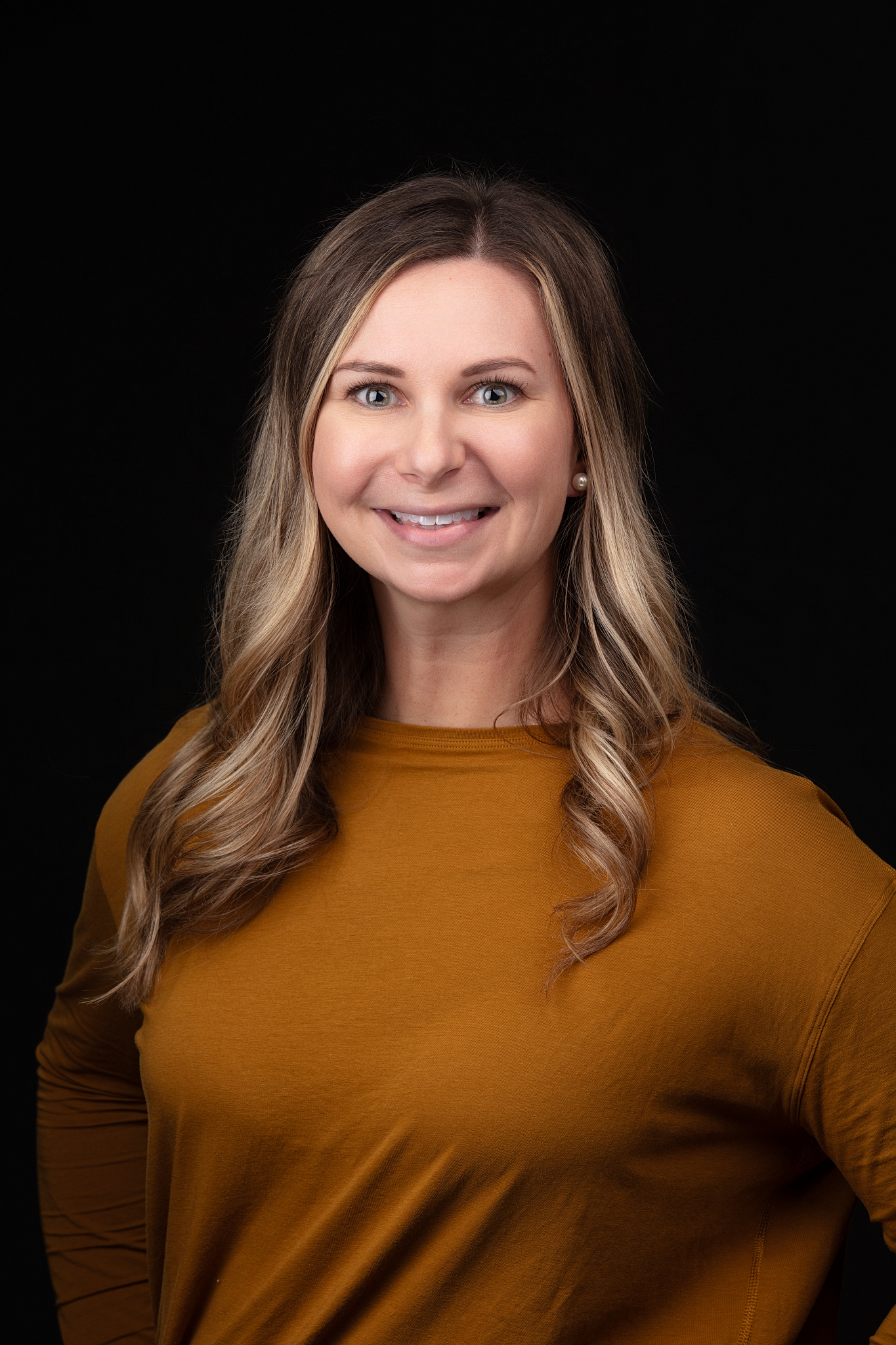Professional headshot of a smiling woman in a mustard sweater on a black backdrop