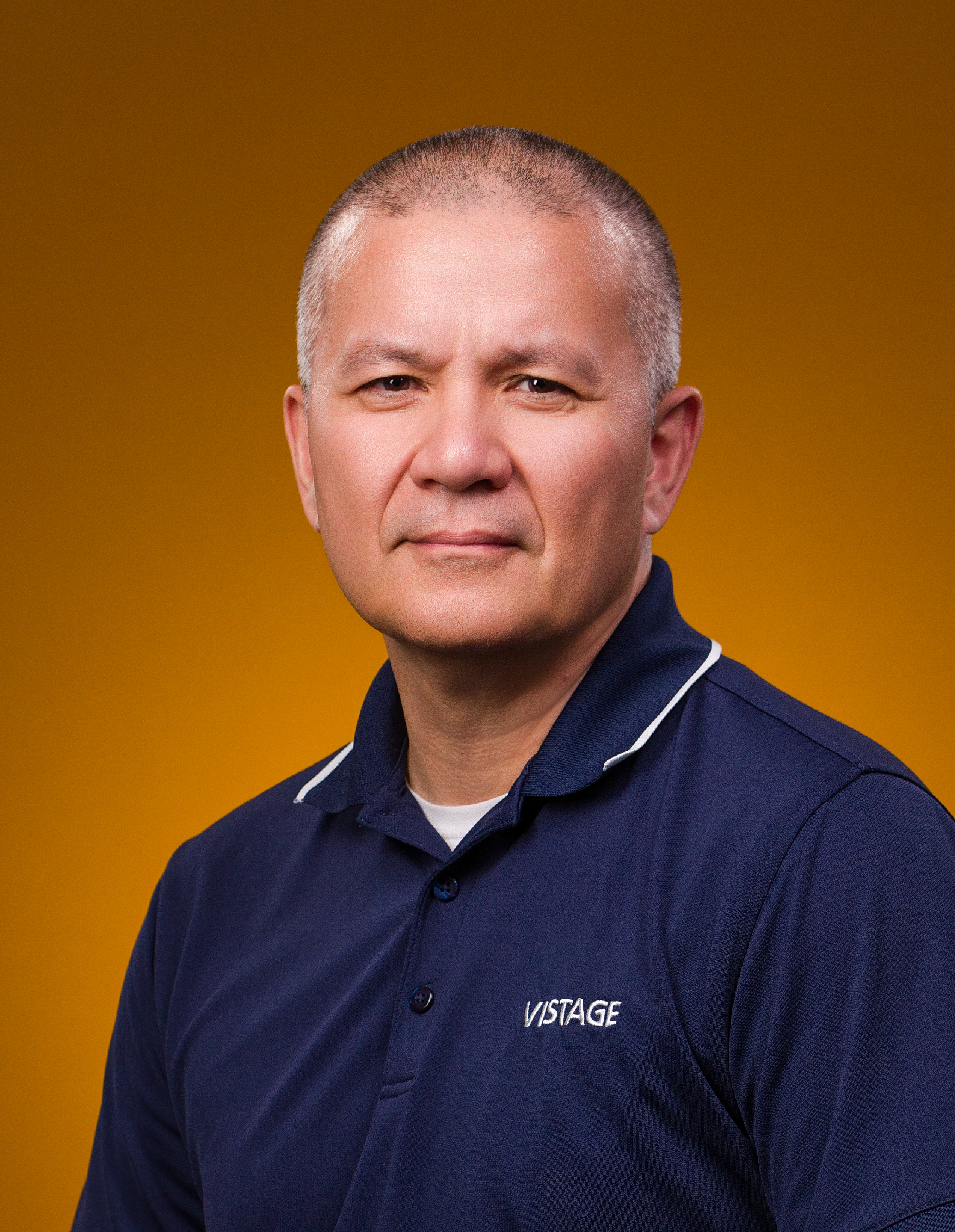 Business headshot of a man in a navy polo shirt against an amber backdrop