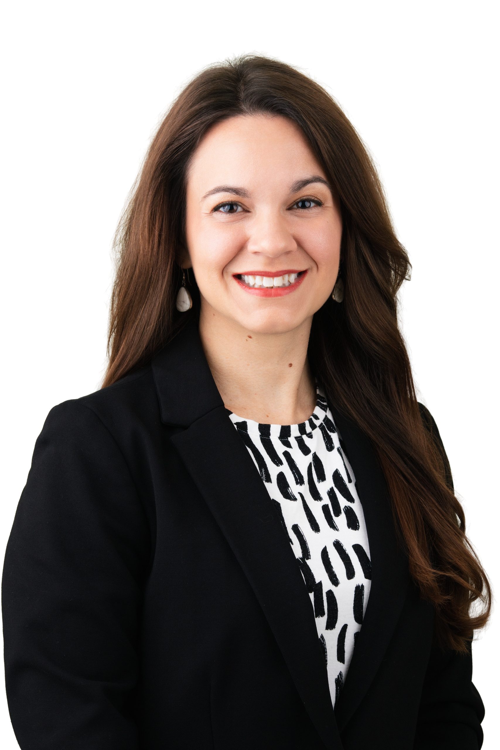 Professional headshot of a smiling woman with long brown hair in a black blazer over a patterned blouse on a white backdrop