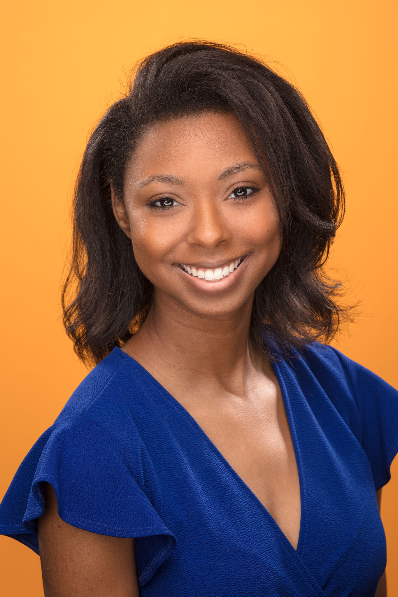 Studio headshot of a smiling woman in a cobalt blue top against an orange backdrop