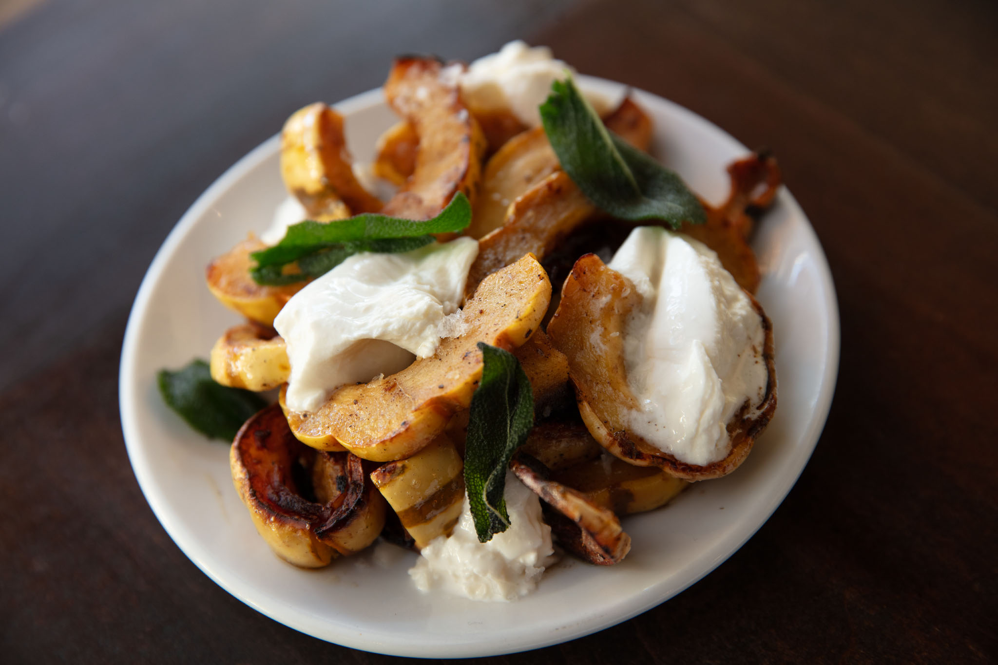 Roasted squash slices with dollops of fresh cheese and crisp sage leaves on a small white plate