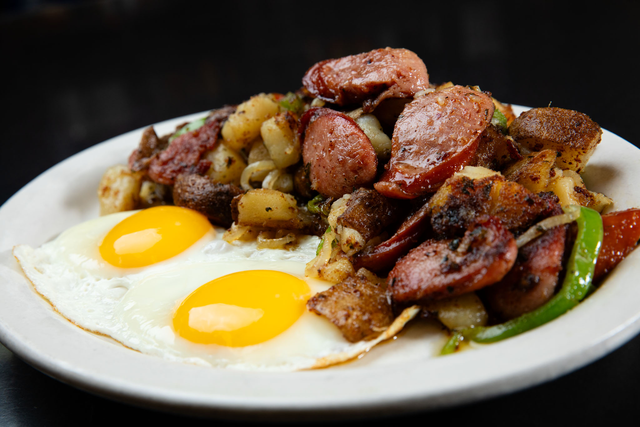 Breakfast plate at Katie Country Kitchen with two sunny-side-up eggs, sliced sausage and skillet potatoes with peppers and onions