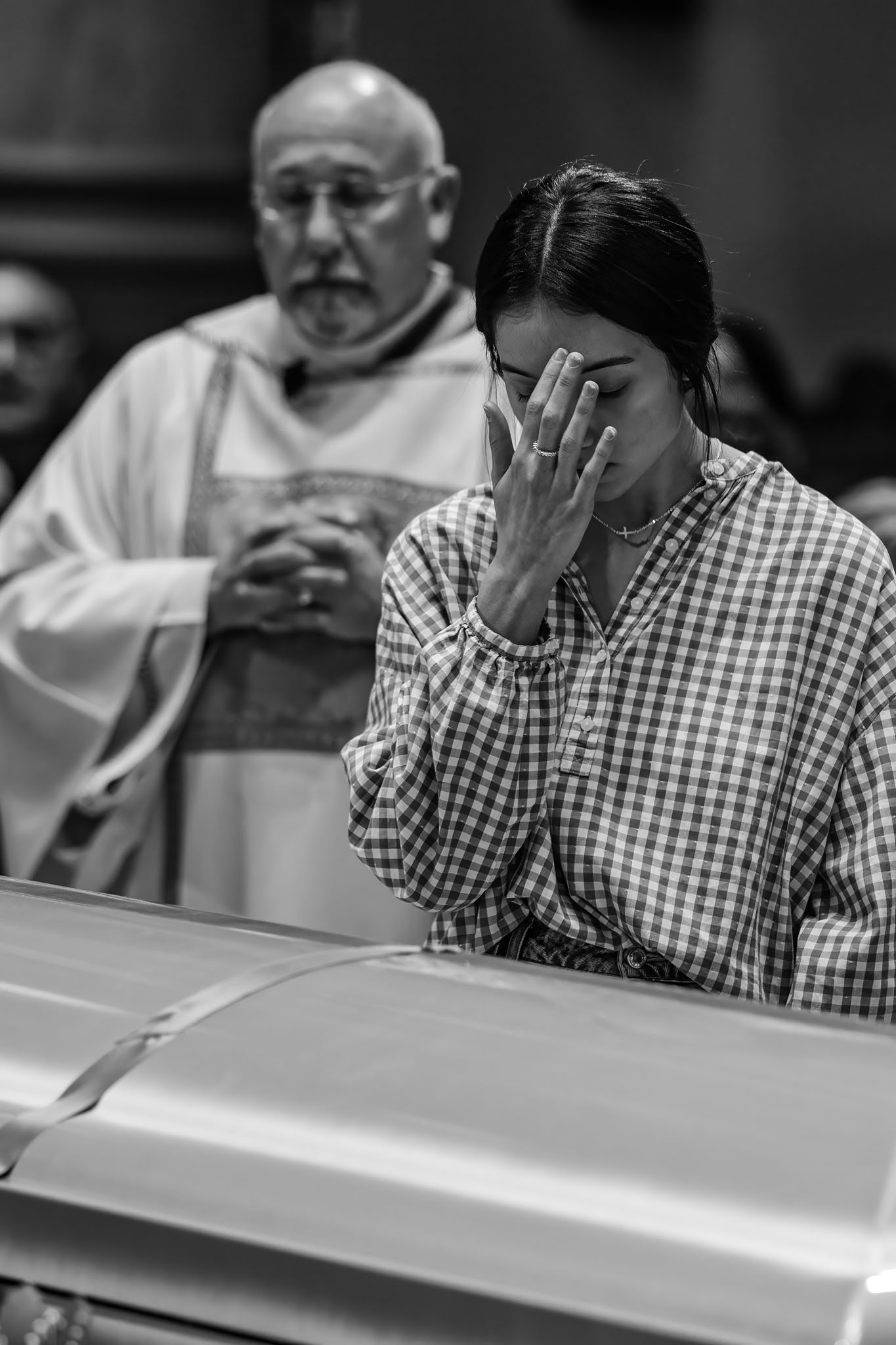 Woman bowing her head in prayer at the casket beside a priest