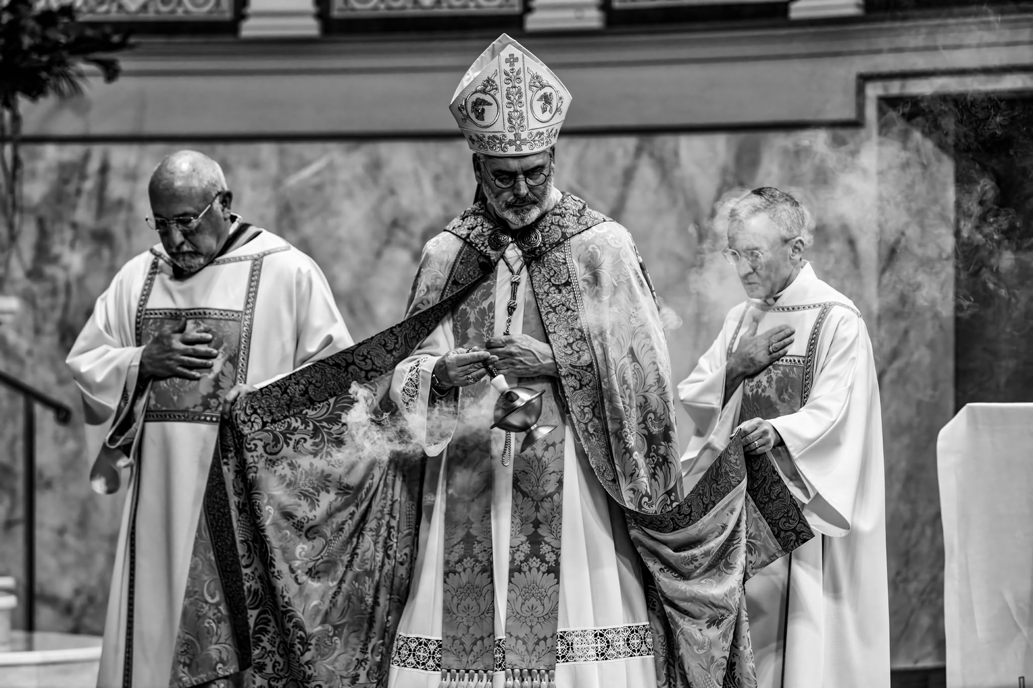 Archbishop in a miter and vestments flanked by clergy at the altar