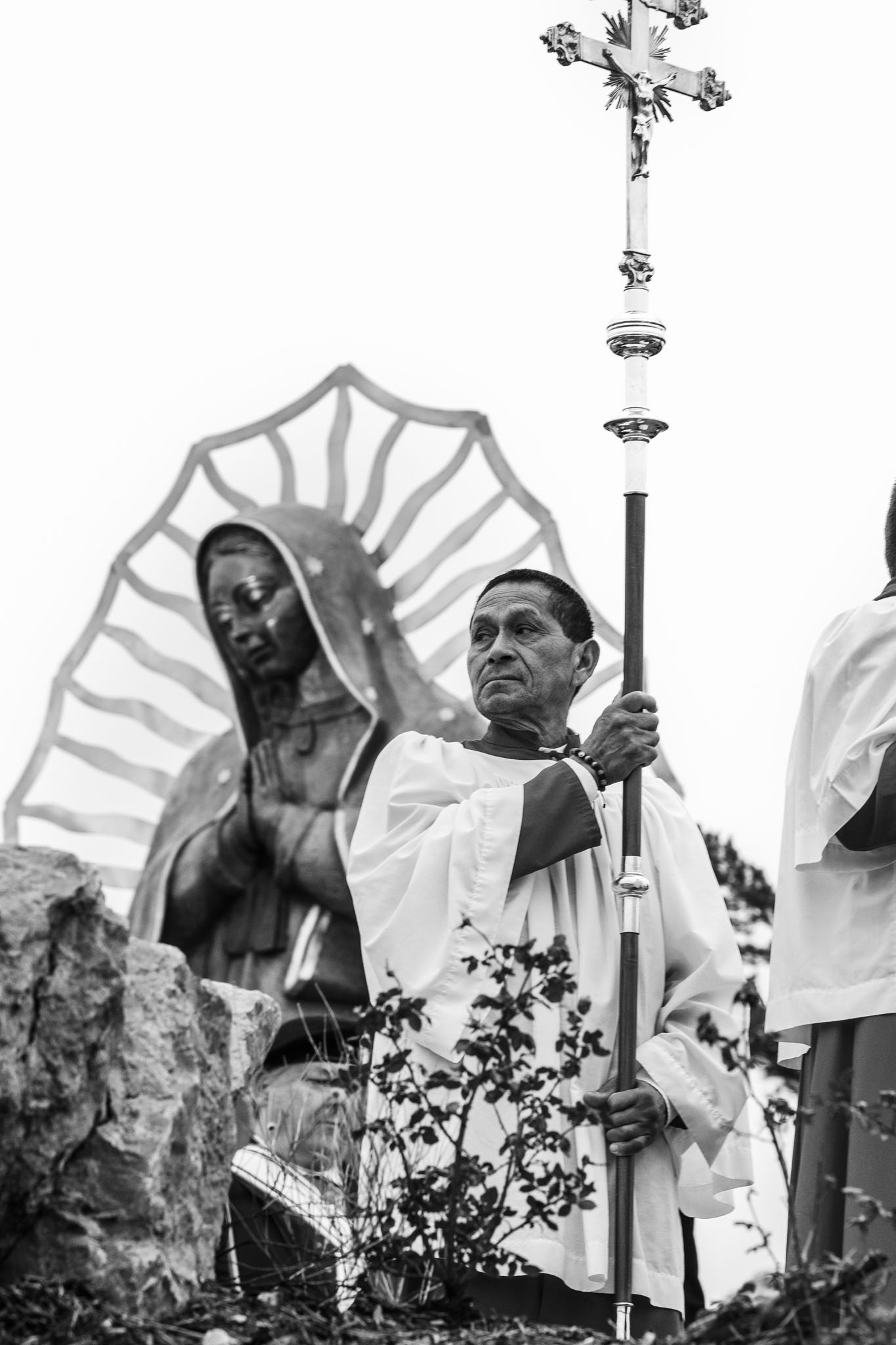 Altar server carrying a processional cross past the statue of Our Lady of Guadalupe
