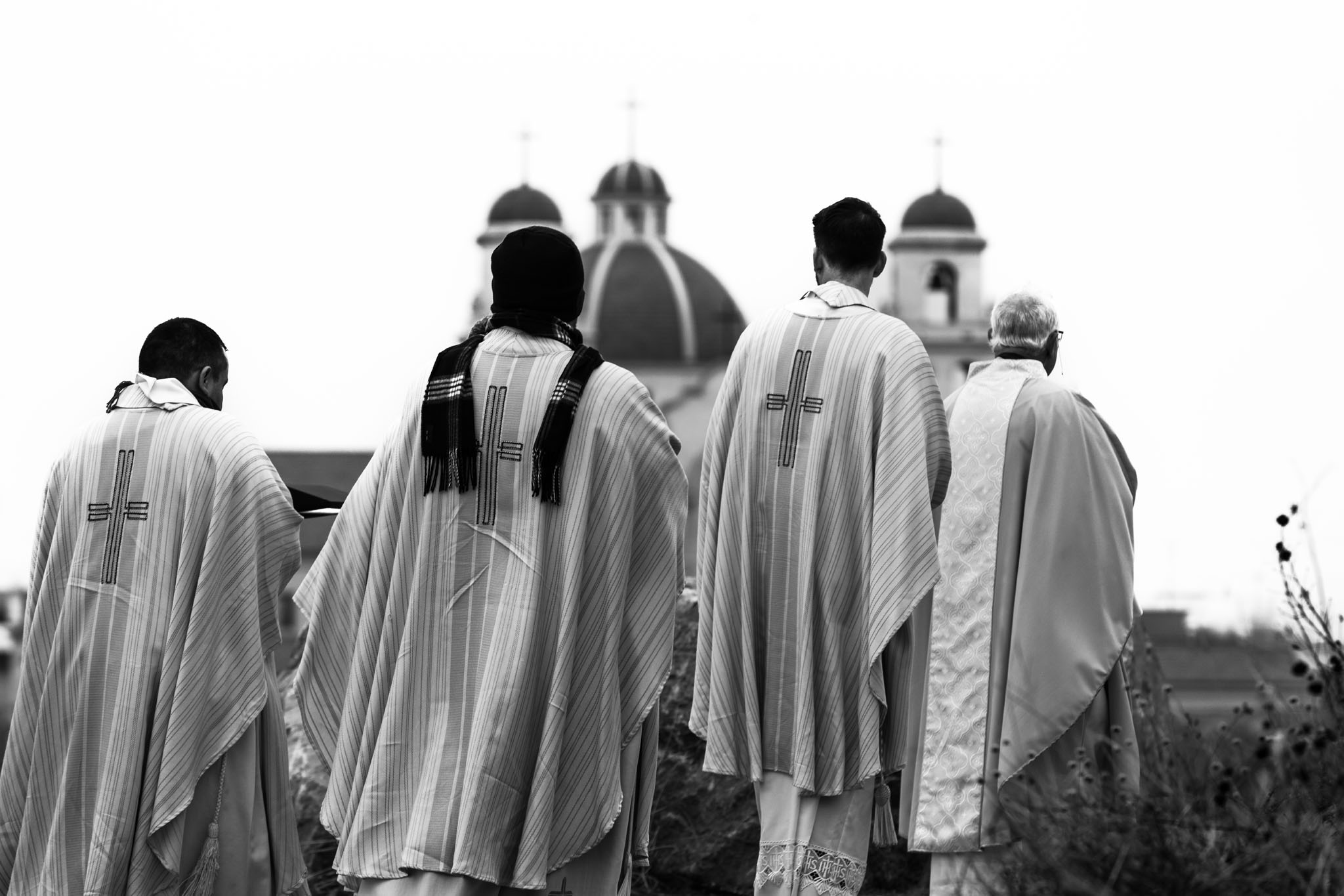 Clergy in white vestments walking toward the shrine’s domes and bell towers