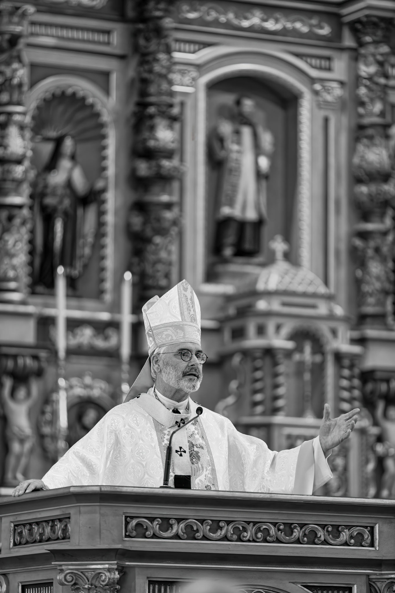 Archbishop in a miter speaking before the shrine’s carved retablo