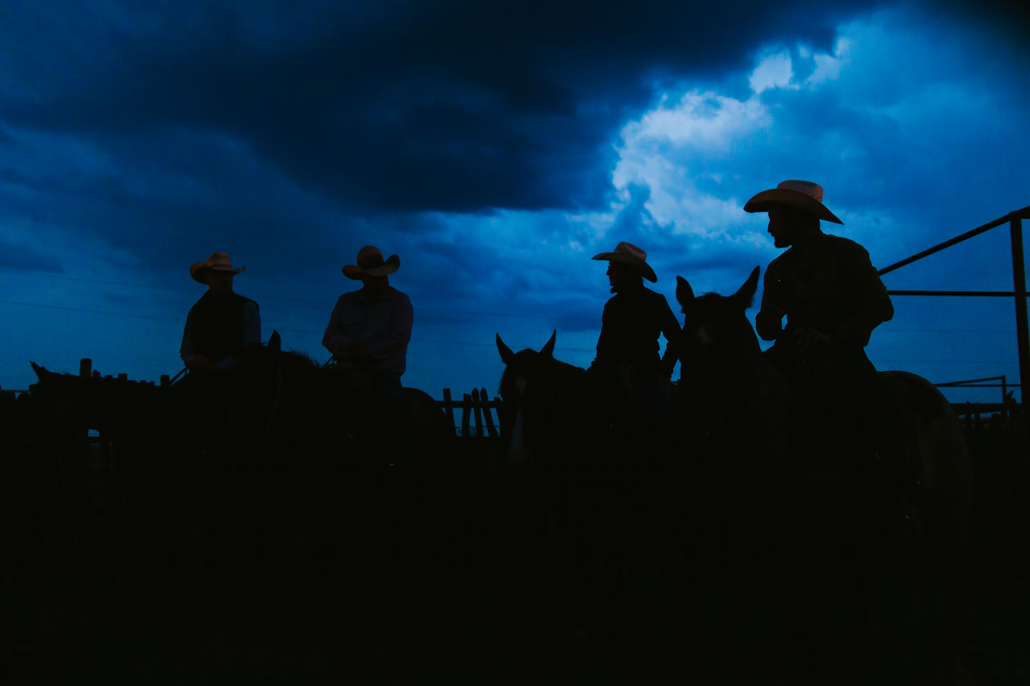 Cowboys on horseback silhouetted against a dark blue storm sky at Stuart Ranch