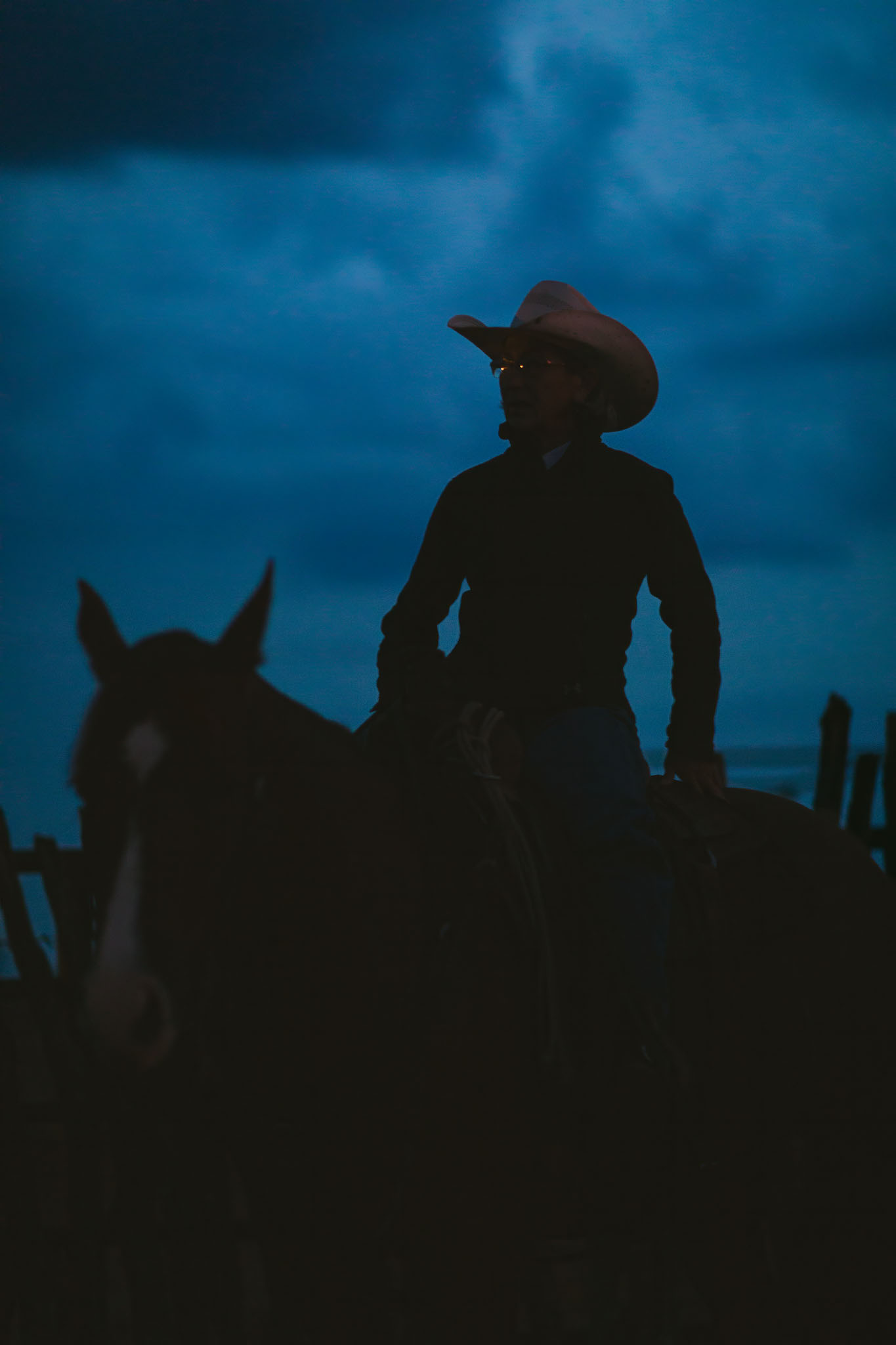 Cowboy on horseback silhouetted against a deep blue early morning sky