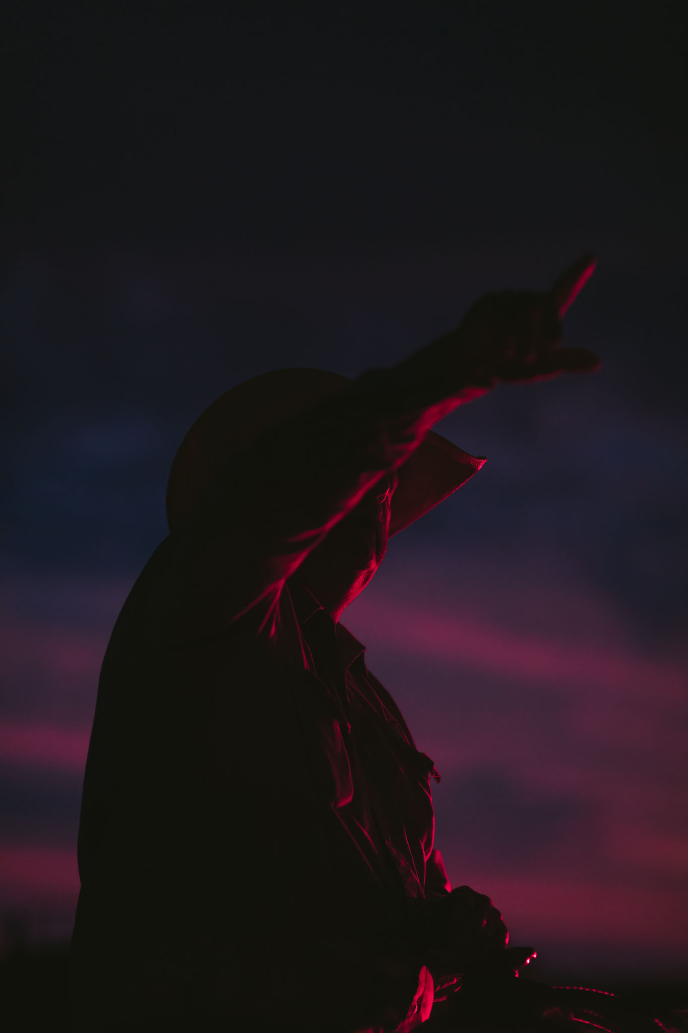 Silhouette of a cowboy raising his arm against a magenta sky